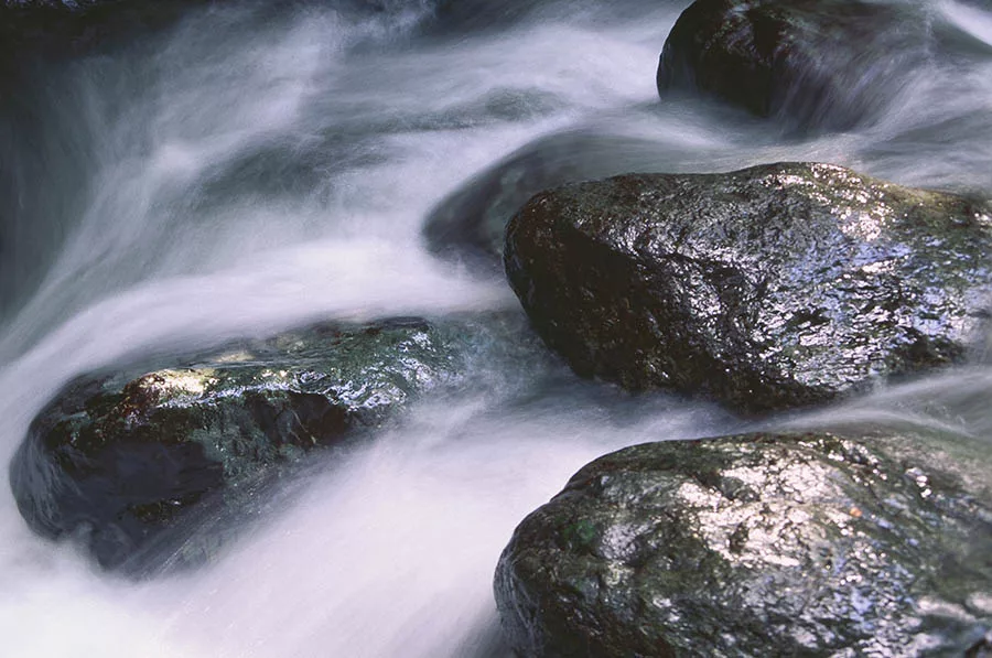 Water rushing between rocks in a small creek to demonstrate sustainable investing.