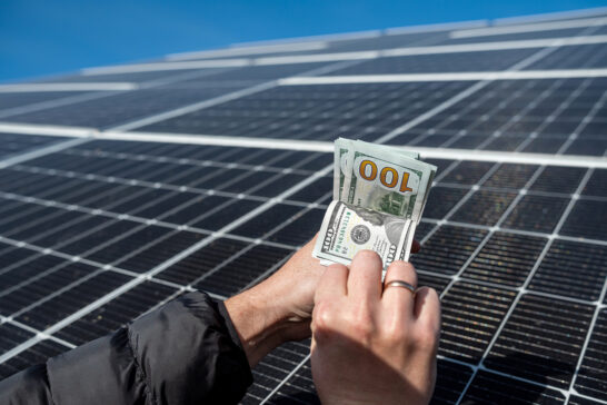 Hand holding cash in front of solar panels, passive income concept to demonstrate the Best Ways to Earn Passive Income